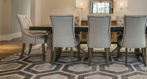 A dining room featuring a rectangular wooden dining table with six upholstered chairs, centered on a transitional area rug with a geometric hexagonal pattern in shades of beige, brown, and grey
