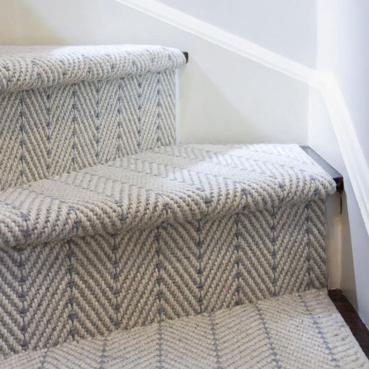 Light gray herringbone-patterned carpet on wooden stairs with white walls, showing modern home interior flooring design